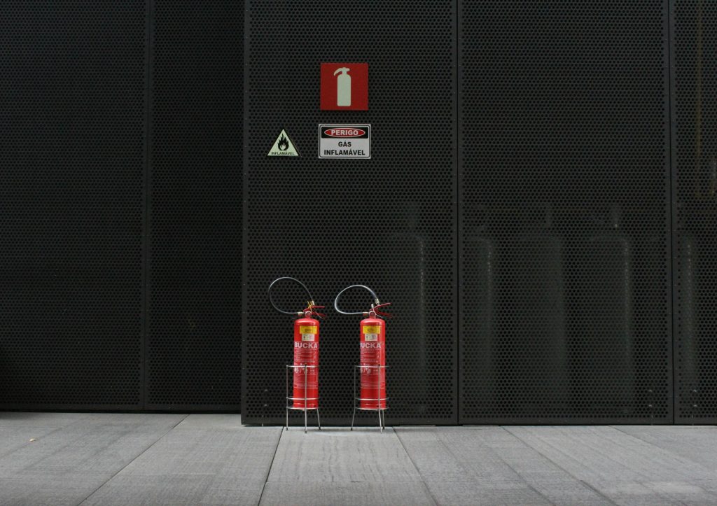 Red fire extinguishers against industrial metal wall with warning signs.